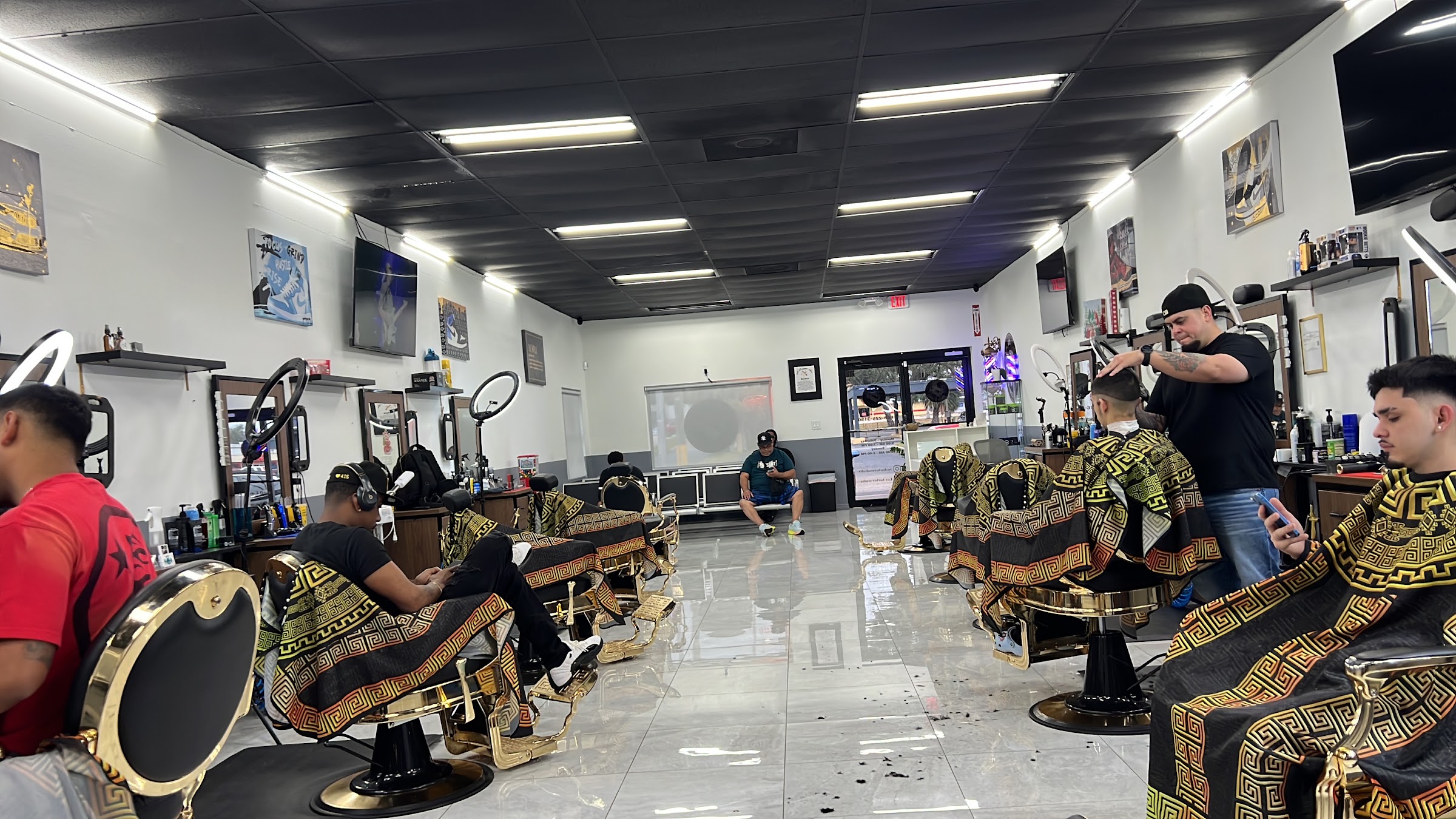 The studio floor at Lux Barber Studio, gold and black chairs on white tile with ring lights at every station
